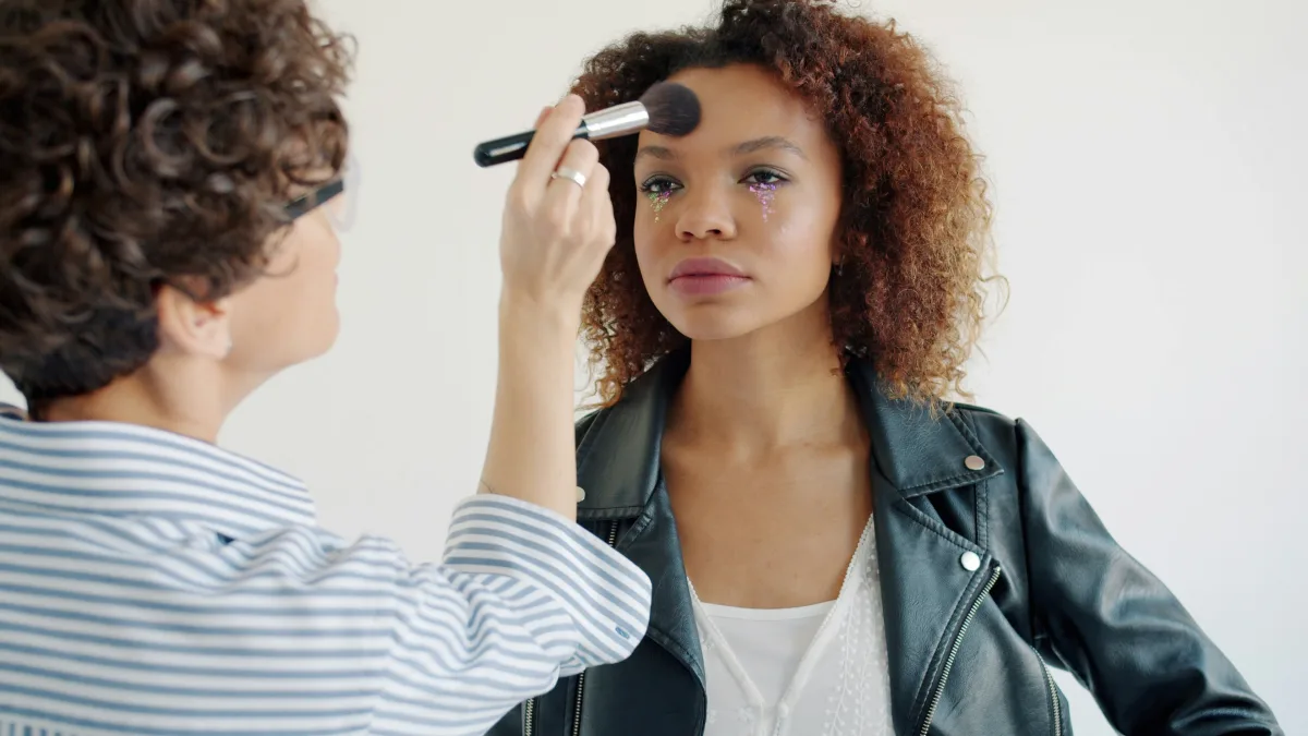 A makeup artist applying face powder with glitter under-eye makeup on a client