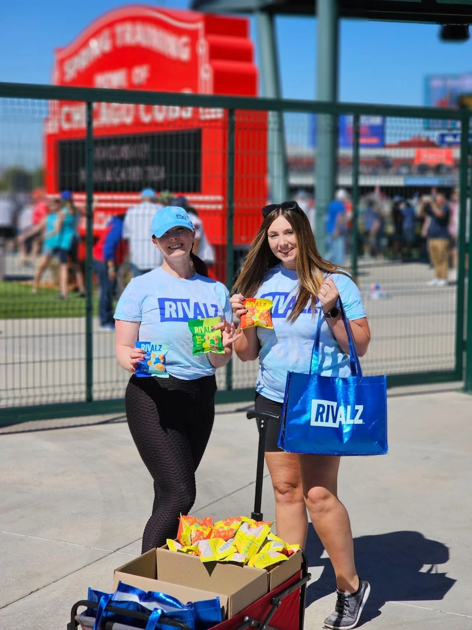 A couple of women holding bags and a cart of snacksDescription automatically generated