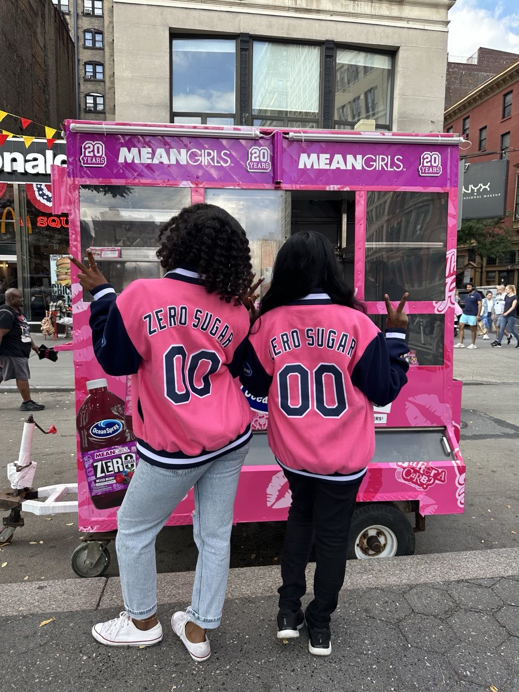 Friends posing at a branded Ocean Spray x Mean Girls street cart activation in New York City